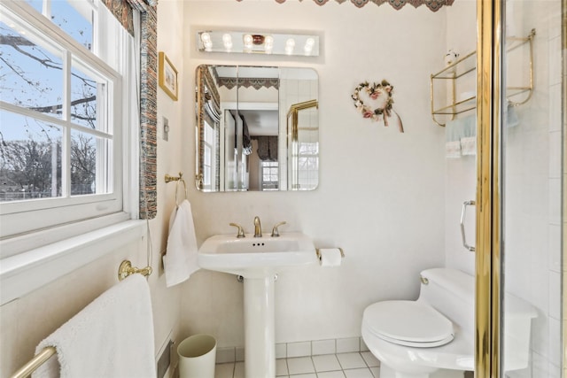 bathroom with toilet, a shower with shower door, tile patterned flooring, and baseboards