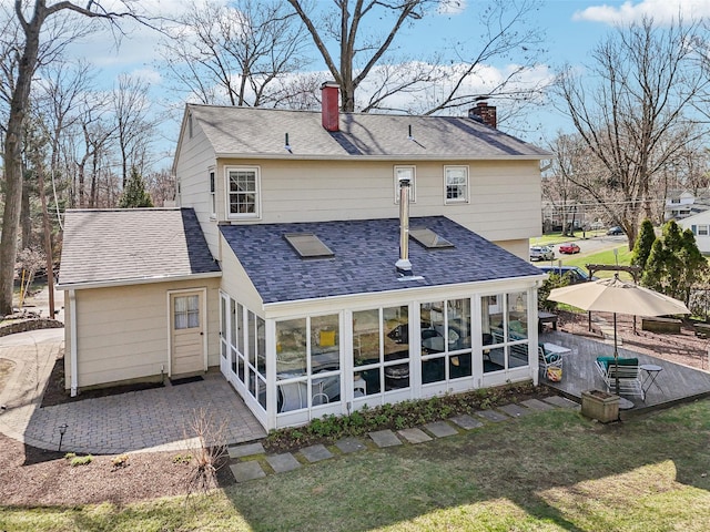 back of house with a lawn, roof with shingles, a chimney, and a sunroom