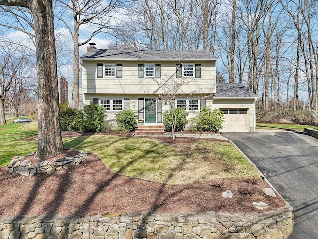 colonial house with a chimney, a garage, entry steps, driveway, and a front yard