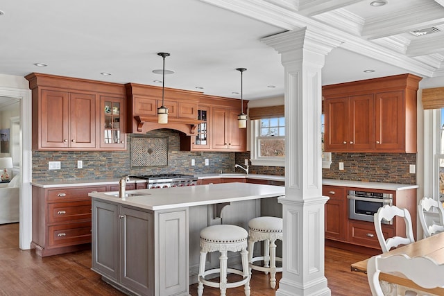 356 Bay Ave, Huntington Bay, NY 11743 - kitchen featuring decorative columns, glass insert cabinets, light countertops, a center island with sink, and dark wood-style floors