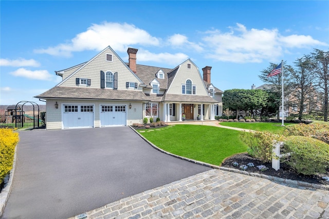 shingle-style home featuring a porch, aphalt driveway, a chimney, fence, and a front lawn