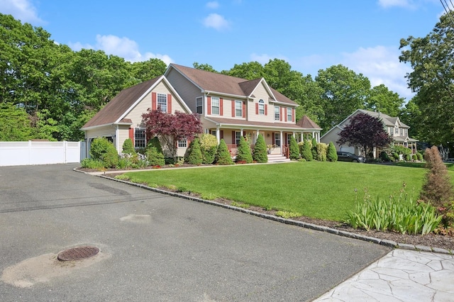 colonial house with a garage, fence, a porch, and a front yard