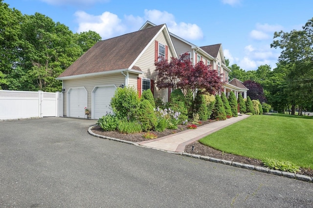 view of side of property featuring a yard, fence, driveway, roof with shingles, and an attached garage