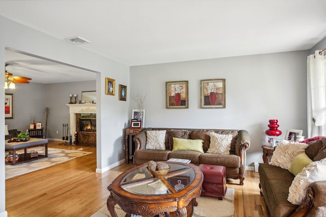 living area with visible vents, a ceiling fan, a premium fireplace, and light wood-style flooring