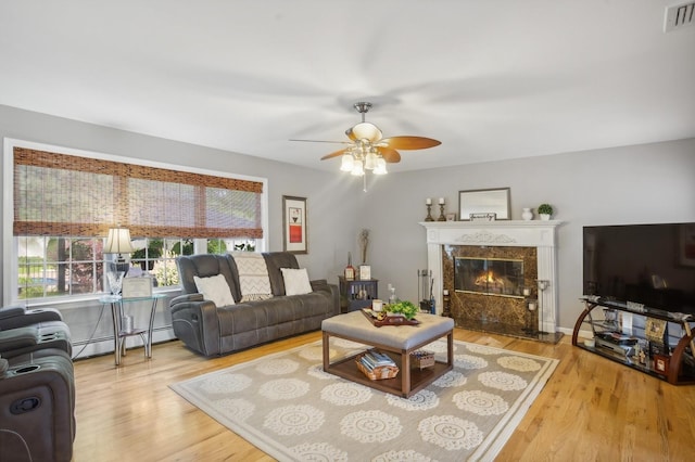 living room featuring visible vents, baseboard heating, a premium fireplace, wood finished floors, and a ceiling fan