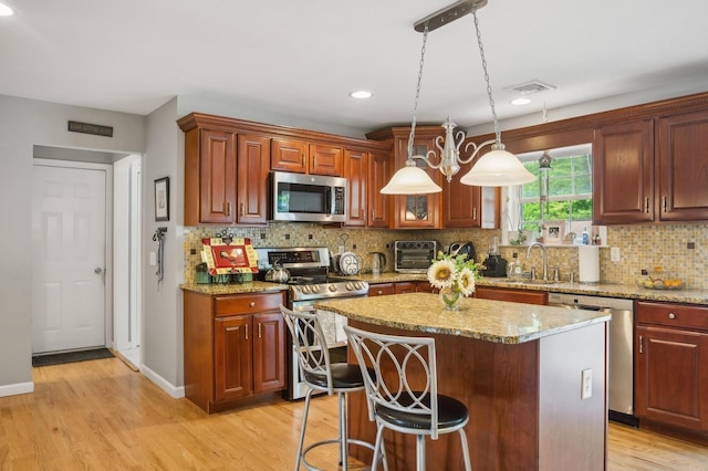 kitchen with light stone counters, a sink, appliances with stainless steel finishes, light wood-style floors, and a center island