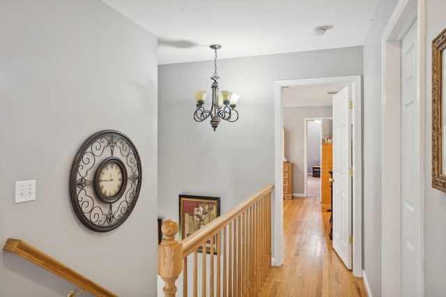 corridor with an upstairs landing, an inviting chandelier, baseboards, and light wood-style floors