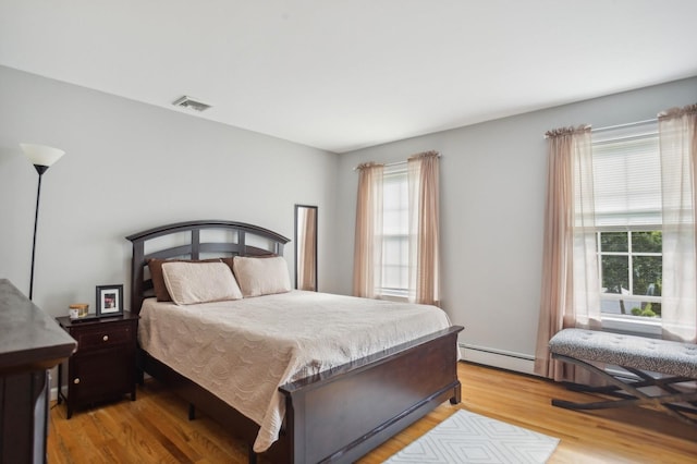 bedroom with visible vents, light wood-type flooring, and a baseboard heating unit