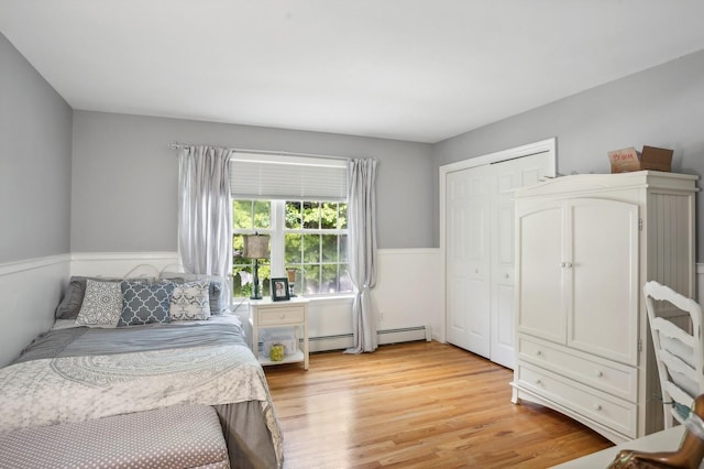 bedroom featuring light wood-style floors, a closet, baseboard heating, and wainscoting