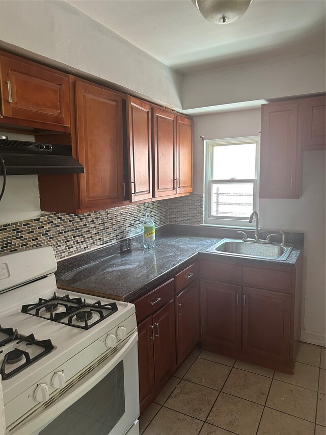 kitchen featuring under cabinet range hood, backsplash, light tile patterned floors, a sink, and gas range gas stove