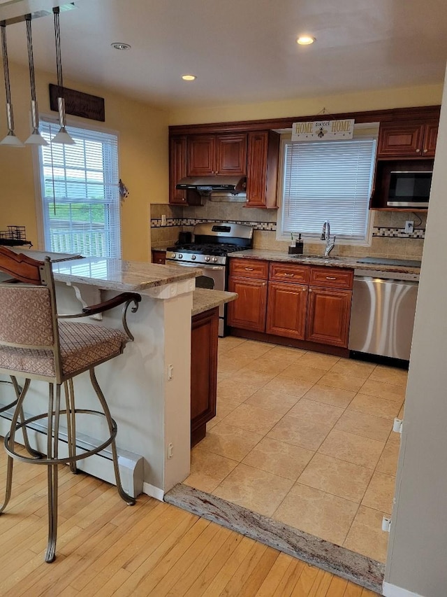 kitchen with stainless steel appliances, a sink, backsplash, light stone countertops, and recessed lighting