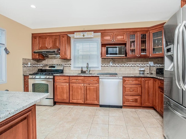 kitchen featuring appliances with stainless steel finishes, a sink, under cabinet range hood, and tasteful backsplash