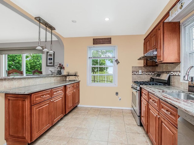 kitchen with appliances with stainless steel finishes, a sink, under cabinet range hood, decorative backsplash, and brown cabinetry
