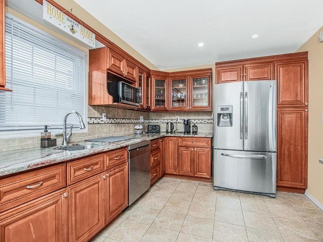 kitchen featuring stainless steel appliances, a sink, light stone countertops, decorative backsplash, and brown cabinetry