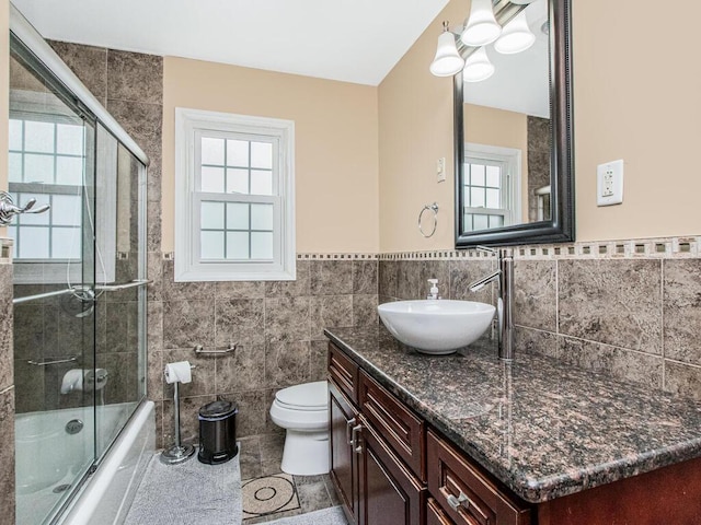 full bath with tile walls, toilet, healthy amount of natural light, enclosed tub / shower combo, and wainscoting