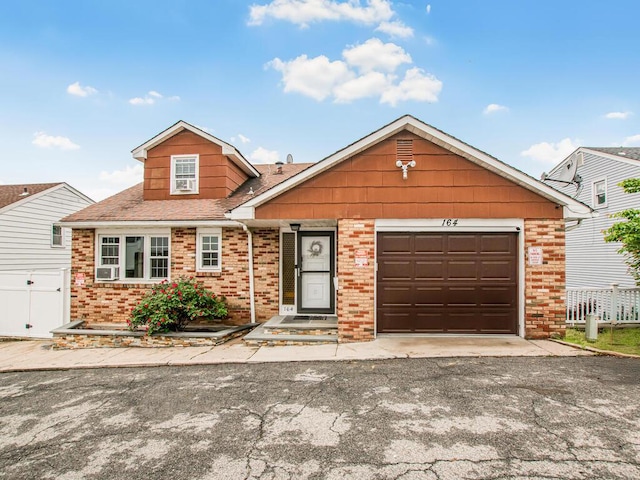 view of front of property featuring brick siding, fence, asphalt driveway, and a garage