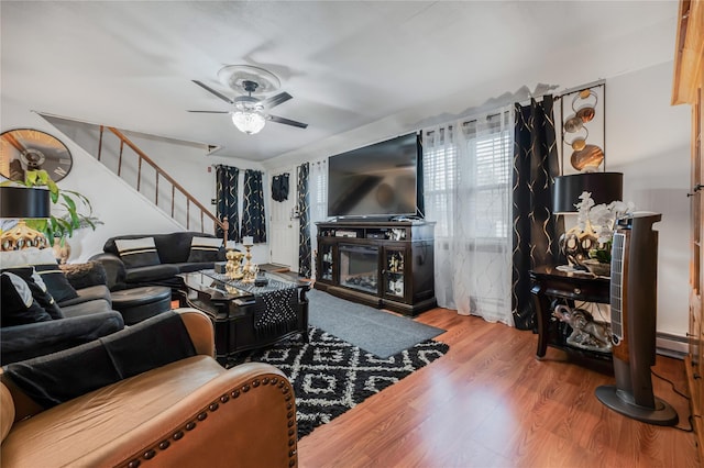 living area with wood finished floors, a ceiling fan, and stairway