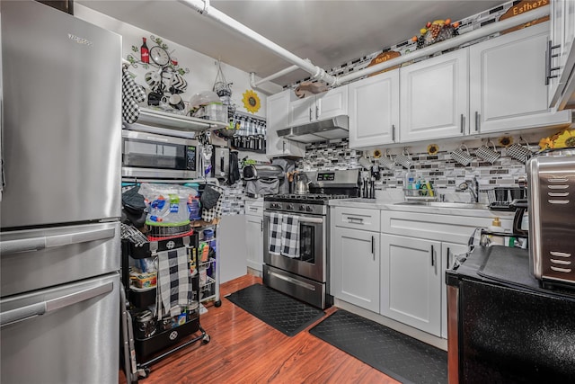 kitchen with white cabinets, under cabinet range hood, appliances with stainless steel finishes, a sink, and wood finished floors