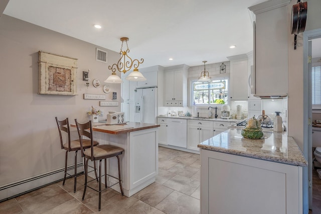 kitchen featuring visible vents, white appliances, a baseboard heating unit, a peninsula, and a kitchen bar
