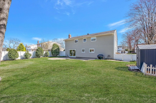 rear view of house featuring a chimney, a fenced backyard, an outdoor structure, a yard, and a patio