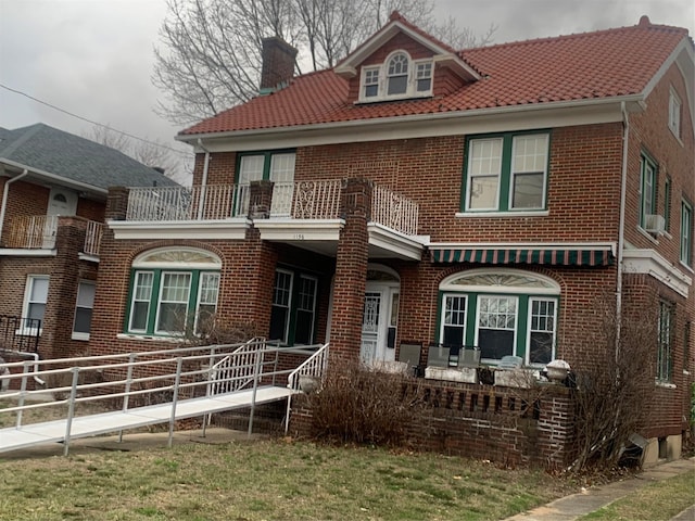 rear view of house featuring covered porch, a chimney, a balcony, and brick siding