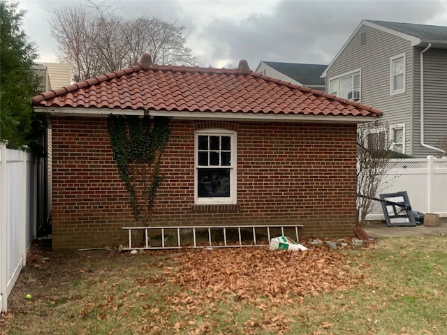 view of side of property with fence, a tiled roof, and brick siding