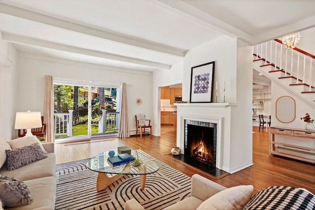 living area with stairway, wood finished floors, a fireplace, and beamed ceiling