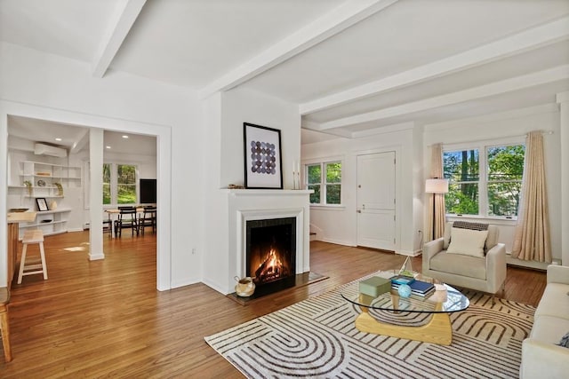 living area featuring baseboards, beamed ceiling, a lit fireplace, and wood finished floors
