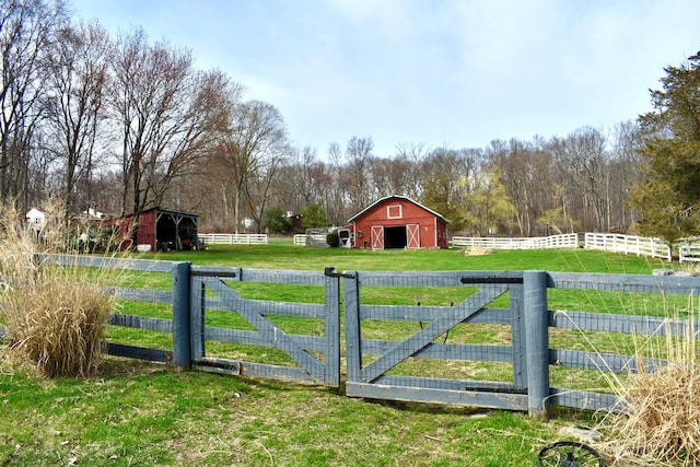 view of gate featuring a barn, an outbuilding, fence, and a yard
