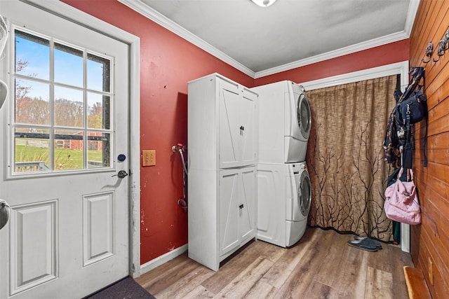clothes washing area featuring baseboards, stacked washer and dryer, crown molding, cabinet space, and light wood finished floors