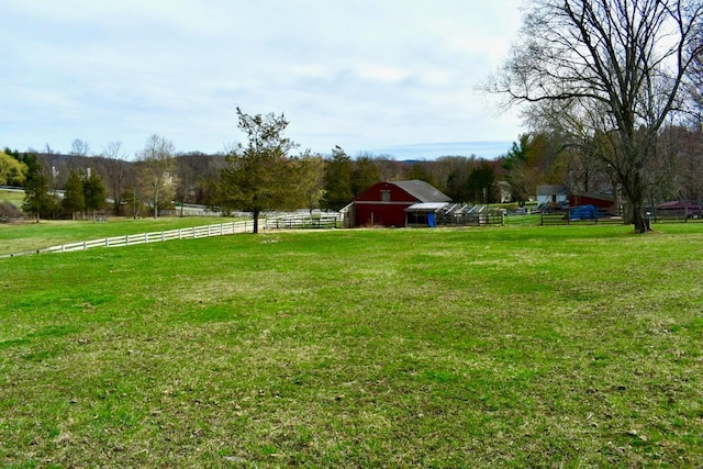 view of yard featuring a rural view, a barn, fence, and an outdoor structure