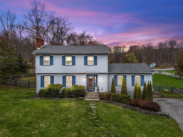 colonial inspired home featuring a yard, roof with shingles, fence, and a chimney
