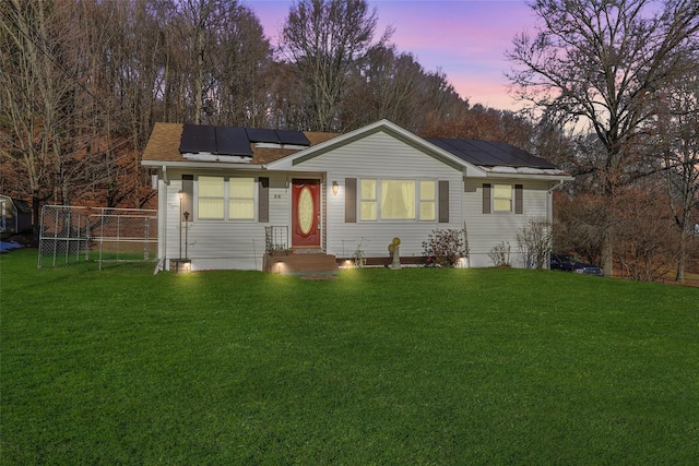 ranch-style home with roof mounted solar panels, fence, and a front lawn