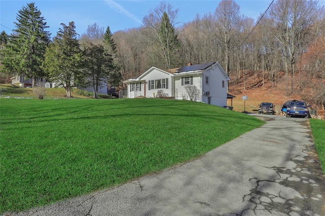 view of front of property featuring aphalt driveway, a front yard, and solar panels
