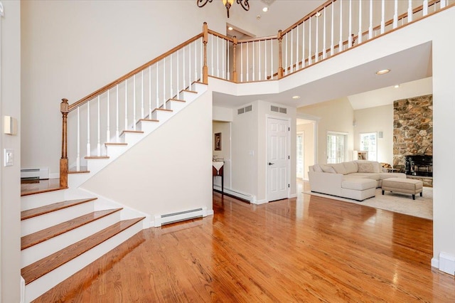 staircase with visible vents, a baseboard heating unit, a high ceiling, and wood finished floors