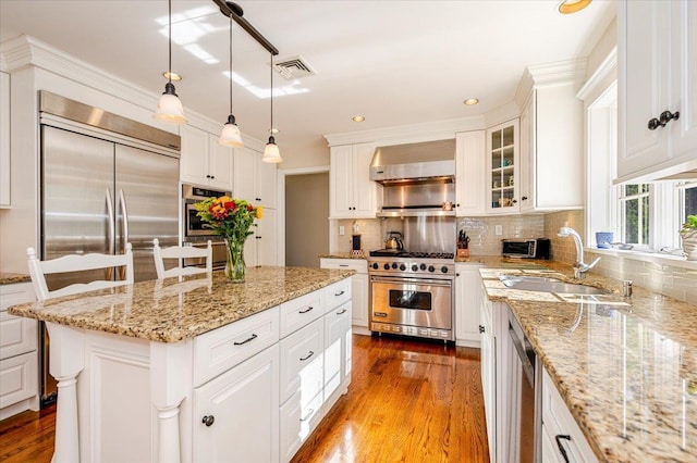 kitchen with wall chimney range hood, white cabinets, stainless steel appliances, a sink, and wood finished floors