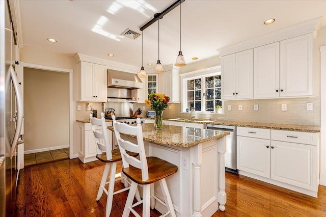 kitchen with appliances with stainless steel finishes, wall chimney exhaust hood, white cabinetry, and visible vents