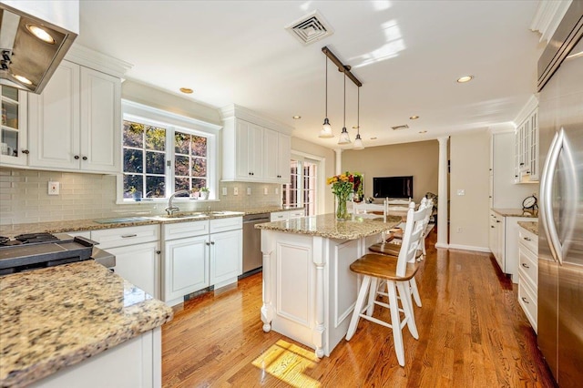 kitchen featuring a center island, white cabinetry, visible vents, stainless steel appliances, and range hood