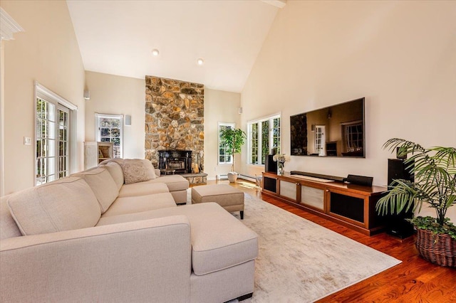 living room featuring wood finished floors, high vaulted ceiling, and a stone fireplace