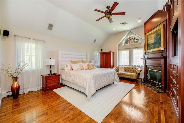 bedroom featuring visible vents, a premium fireplace, vaulted ceiling, and wood finished floors