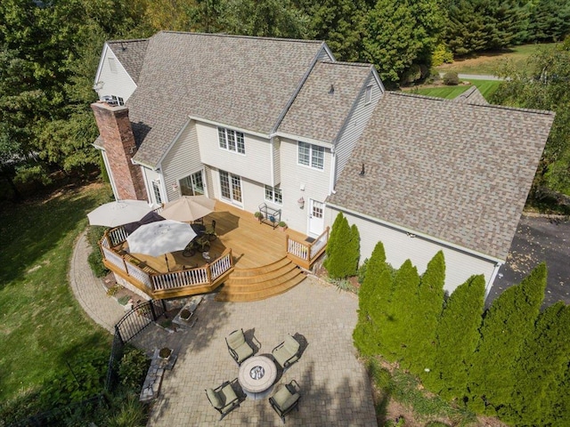 exterior space with a chimney, outdoor dining area, a wooden deck, an outdoor fire pit, and a shingled roof