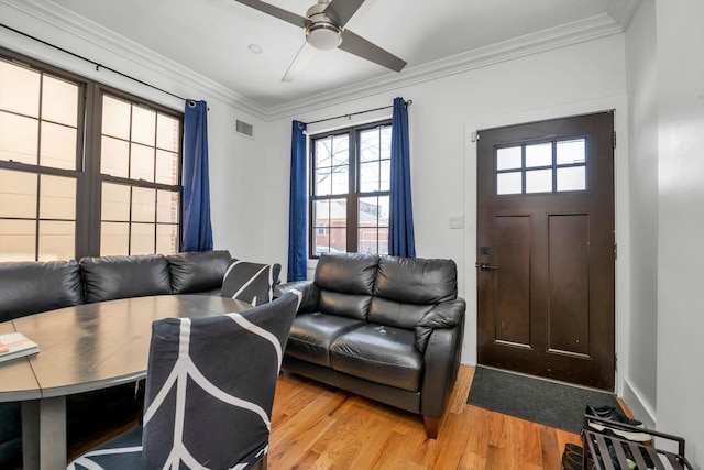 living area with light wood-style floors, visible vents, a ceiling fan, and ornamental molding