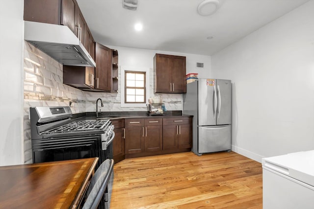 kitchen featuring under cabinet range hood, dark countertops, a sink, stainless steel appliances, and backsplash