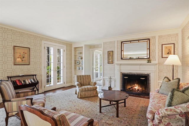 living area with a warm lit fireplace, ornamental molding, built in features, and wood finished floors