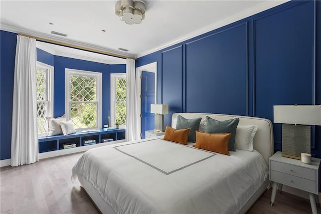 bedroom with a decorative wall, visible vents, ornamental molding, and wood finished floors