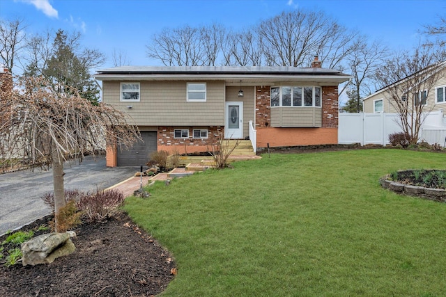 split foyer home with fence, an attached garage, driveway, a front yard, and roof mounted solar panels
