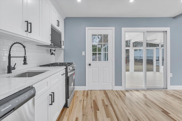 kitchen featuring a sink, light wood-type flooring, light stone counters, and appliances with stainless steel finishes