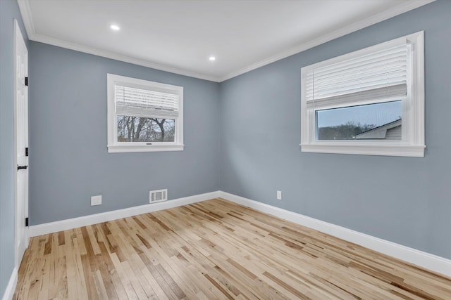 spare room with light wood finished floors, baseboards, visible vents, and ornamental molding