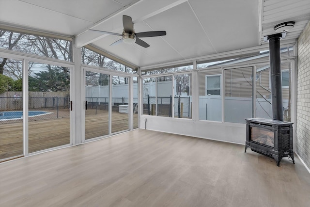 unfurnished sunroom featuring a wood stove, a ceiling fan, and beam ceiling