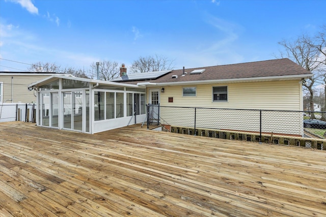 rear view of property with a sunroom, solar panels, fence, and a wooden deck